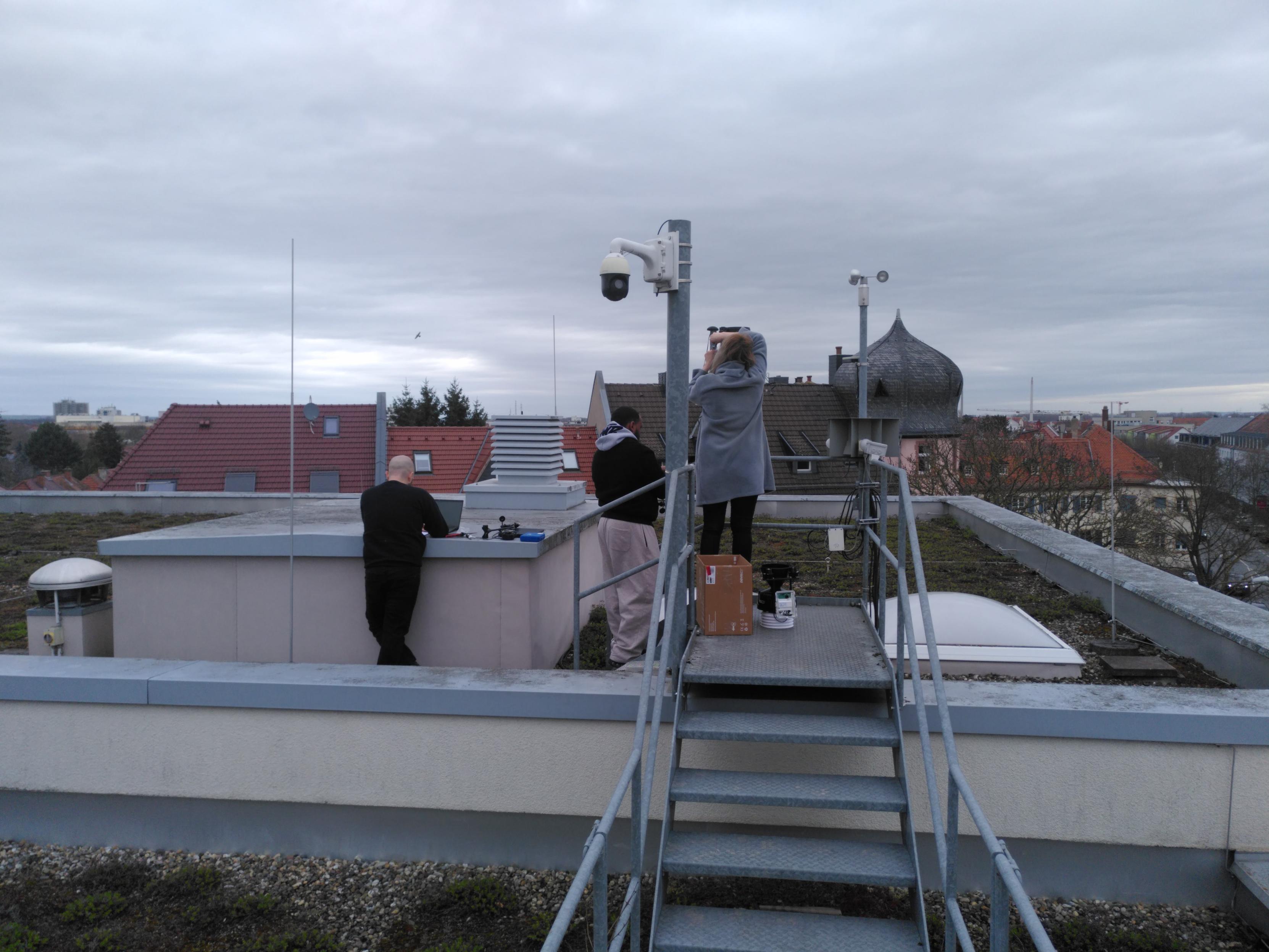 Foto vom Dach der Hochschule Worms: Drei Mitglieder des Projekts WetterStabil (Teamorientiertes Projekt im Bachelor-Studiengang Angewandte Informatik) schrauben die defekten Sensoren der Wetterstation ab, um neue anzuschrauben.